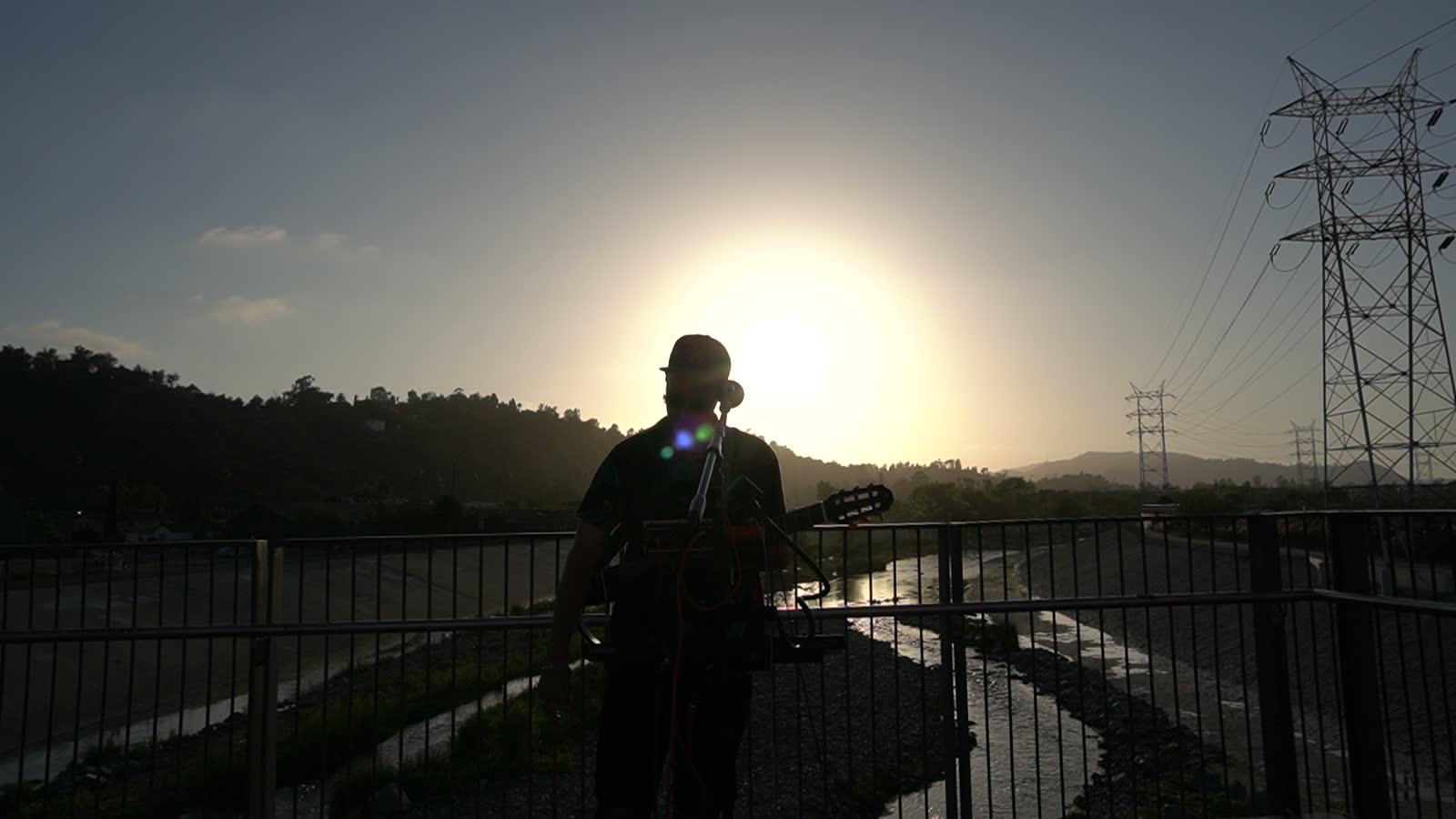 MAGMATIC backlit on the bridge, the sun still high behind him, transmission towers to the right.