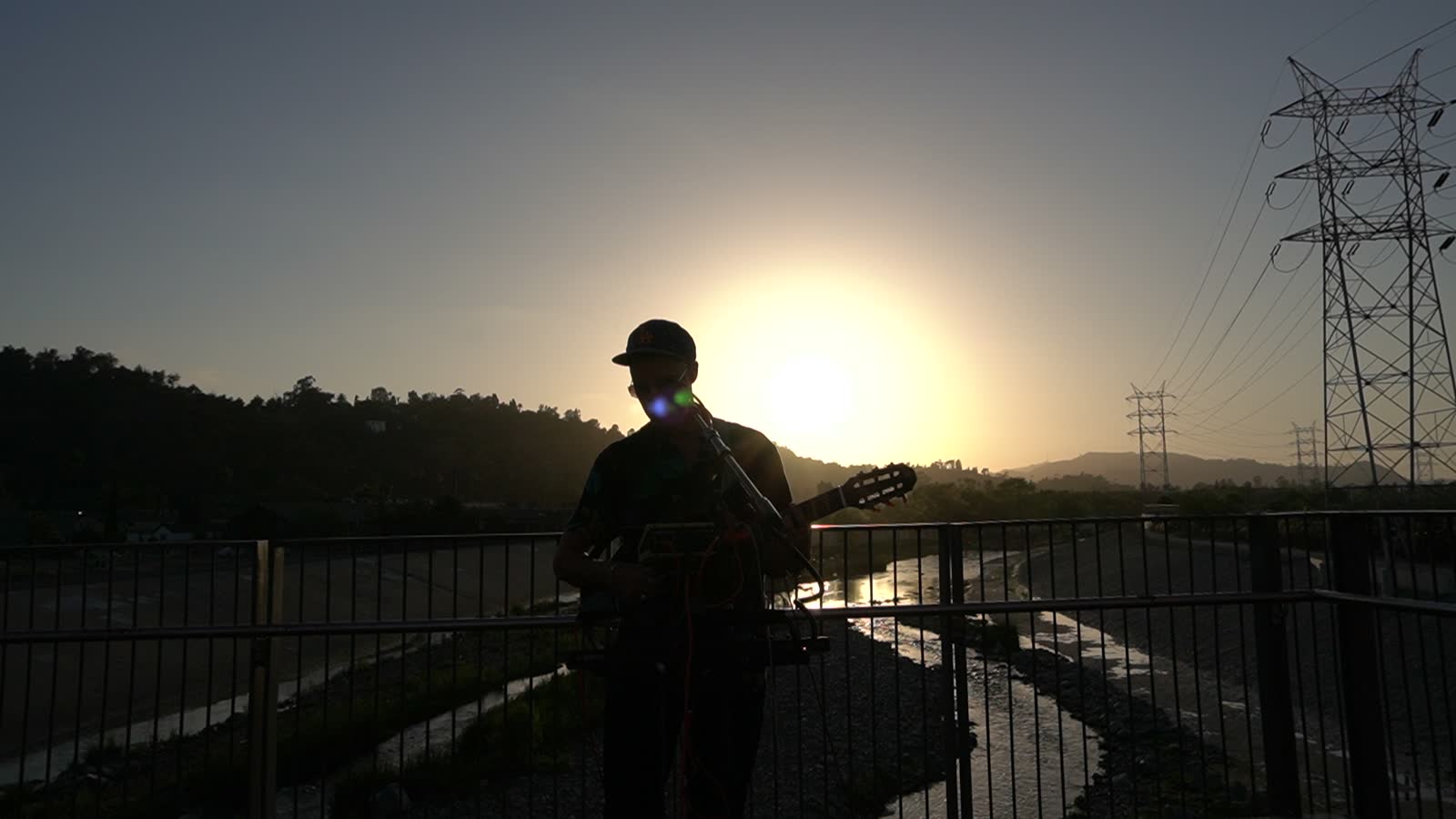 Silhouette of the artist with guitar, the sun sinking toward the hills, golden sky.